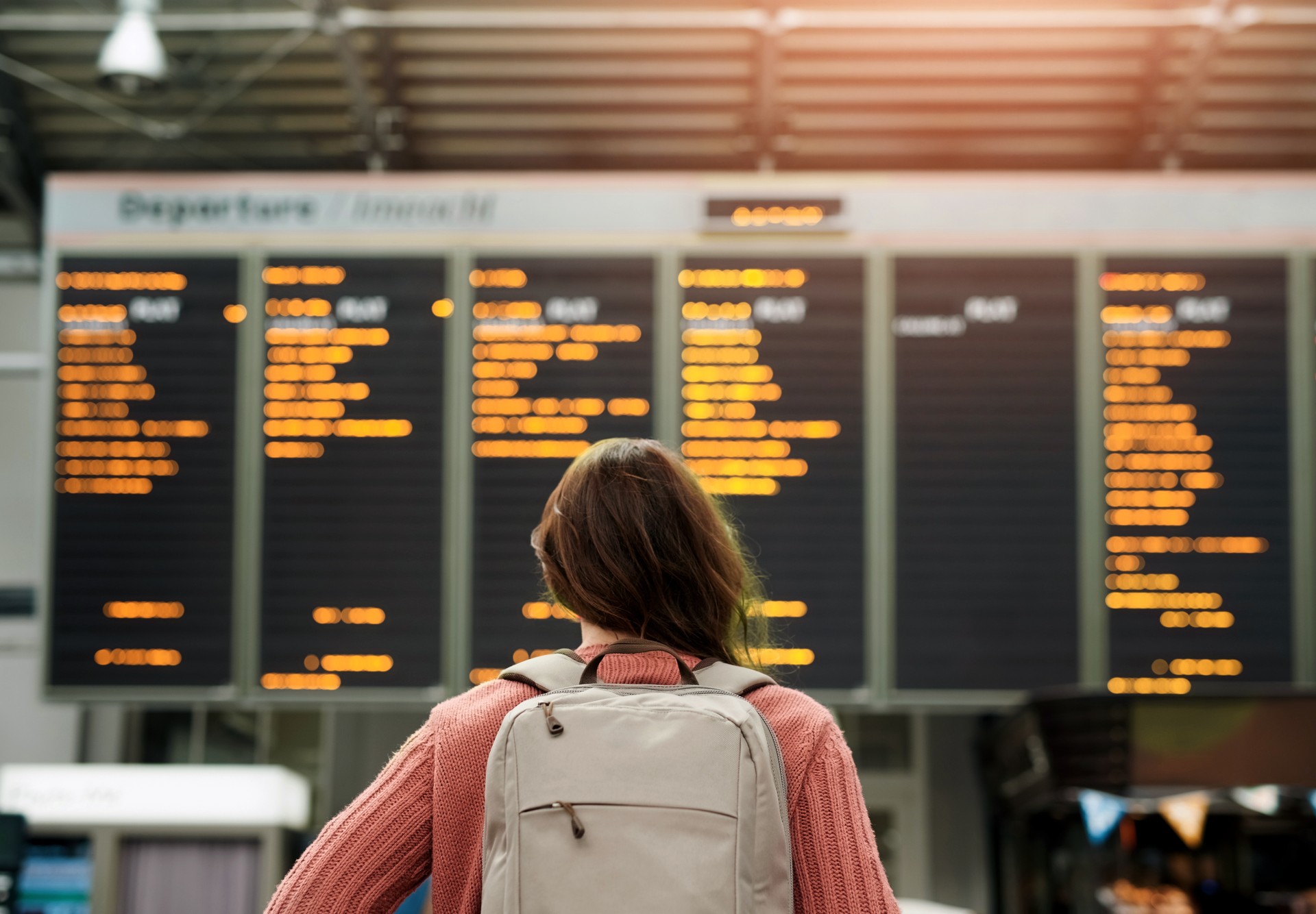 Woman, back and airport with flight schedule on board with information display for global immigration. Person, backpack and international travel with digital time table on screen, location or arrival