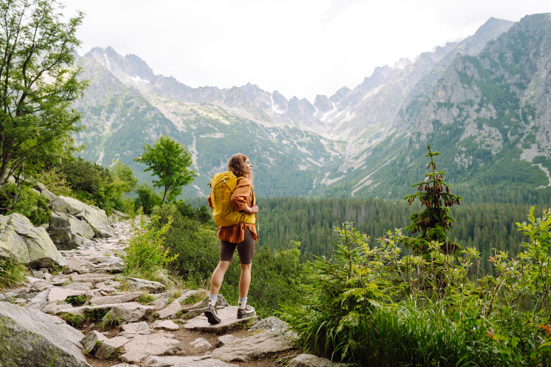 Happy woman with a yellow hiking backpack enjoying the mountain landscape.