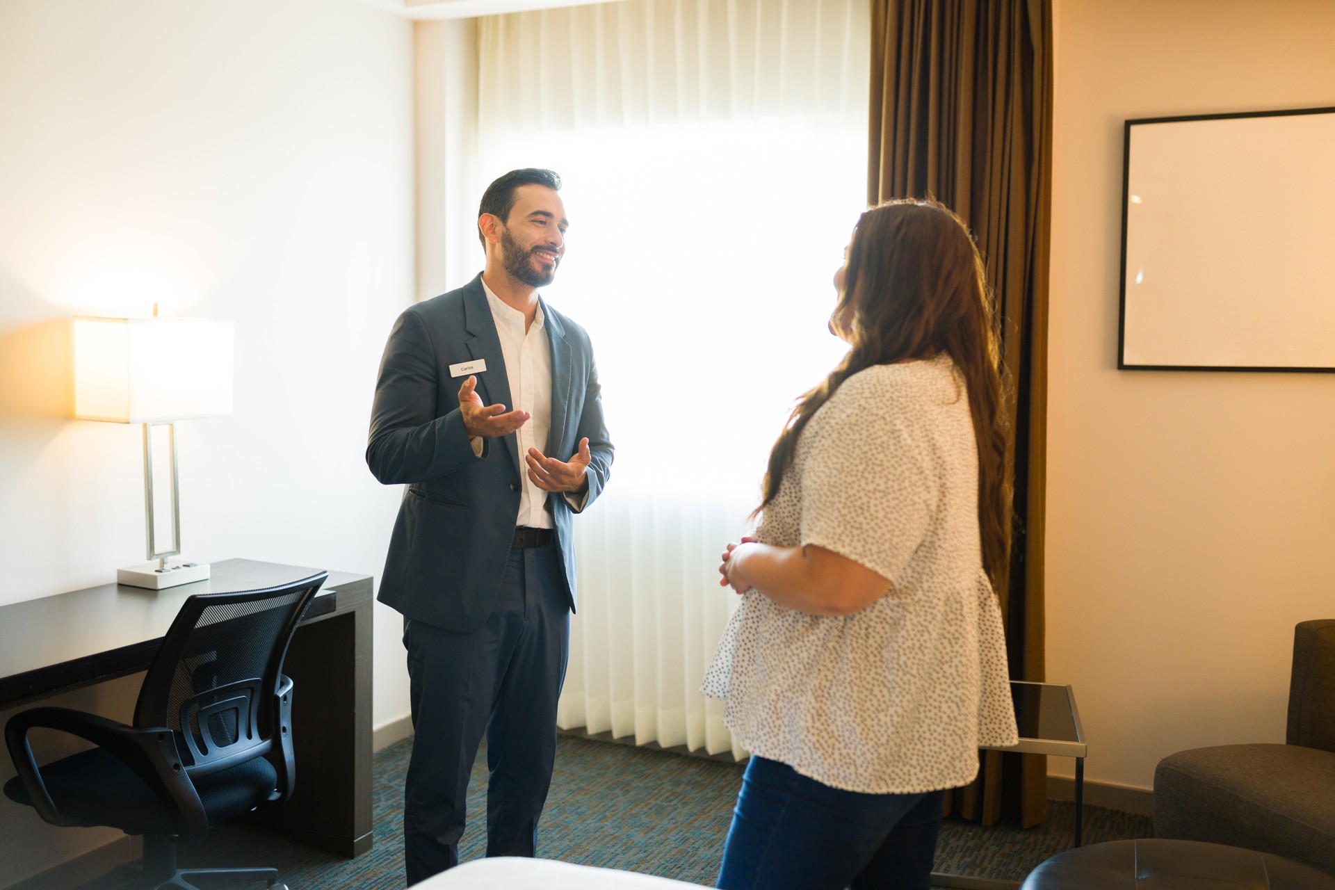 Hotel concierge smiling and using hand gestures to explain room amenities to a female guest